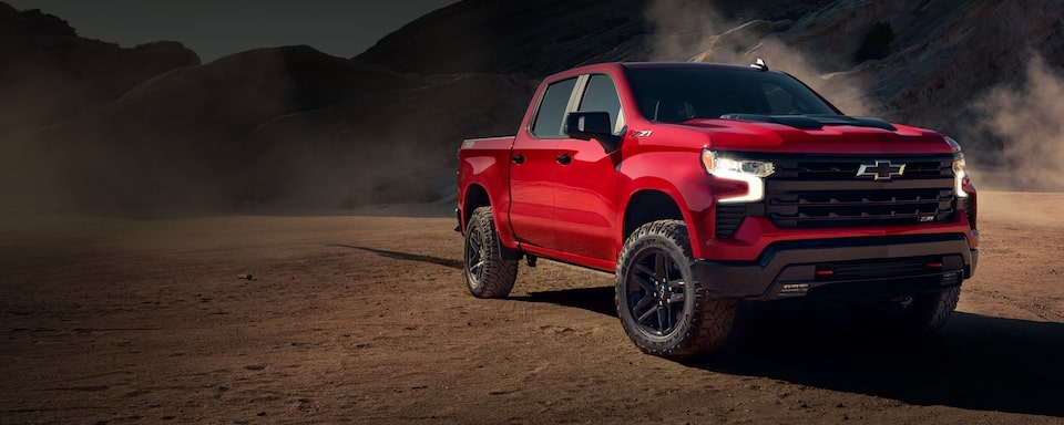 Chevrolet Silverado en un terreno arenoso con montañas de fondo.