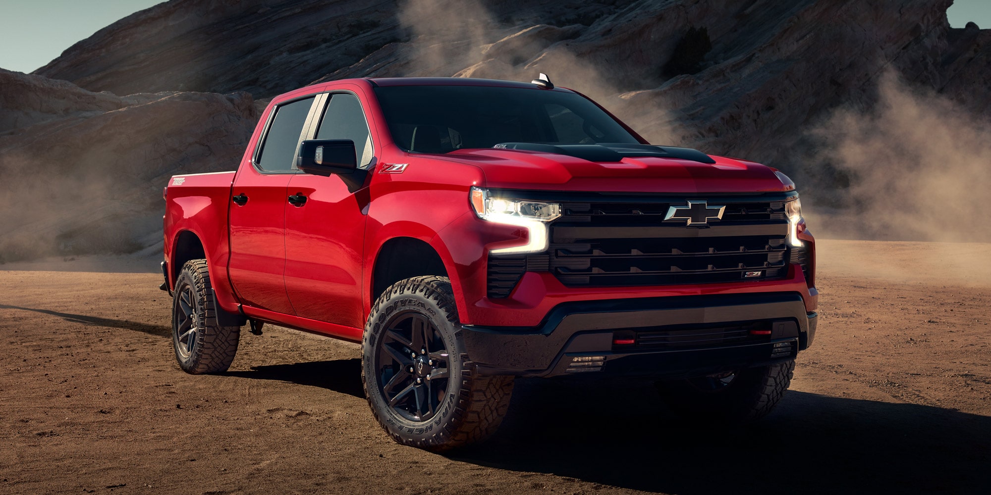 Chevrolet Silverado color Rojo Brillante estacionada en camino de tierra con formaciones rocosas de fondo.
