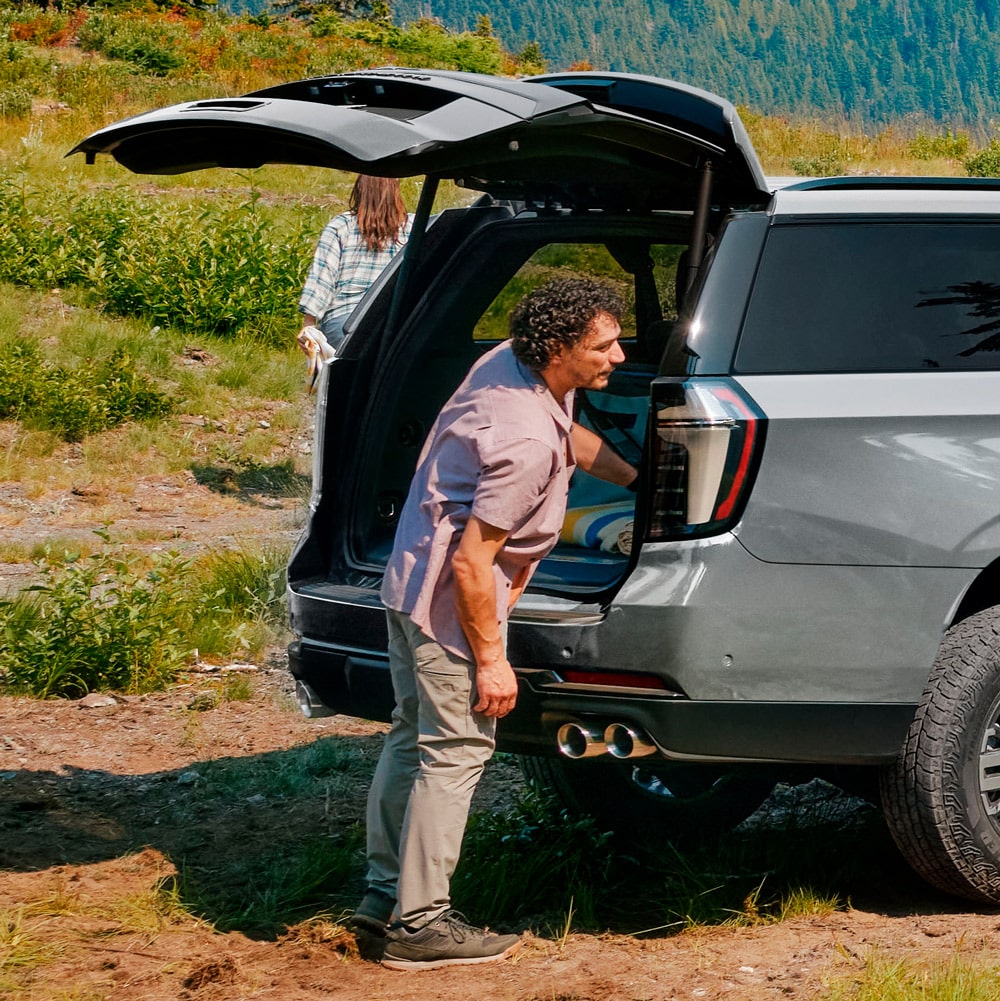 "Hombre utilizando la maletera con apertura eléctrica de la Chevrolet Suburban Z71 en un paisaje natural de montaña. "