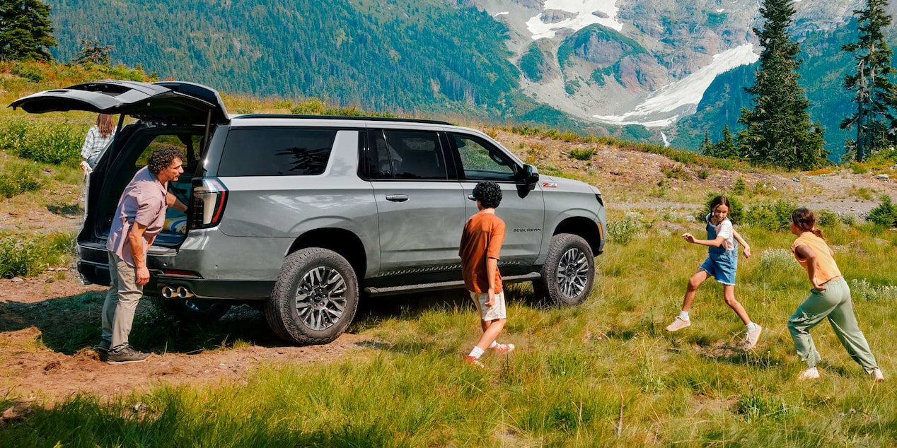 Familia disfrutando al aire libre junto a la nueva Chevrolet Suburban Z71 en color plateado, estacionada en un paisaje montañoso.