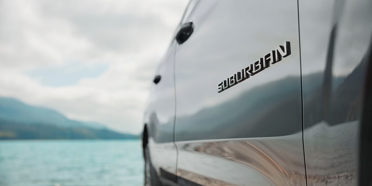 Primer plano de la insignia Suburban en la Chevrolet Suburban Z71, junto a un pasiaje de lago.