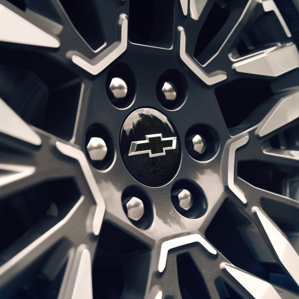 Primer plano de la llanta de aleación de la Chevrolet Suburban Z71 con el emblema de Chevrolet, junto a un paisaje de lago.