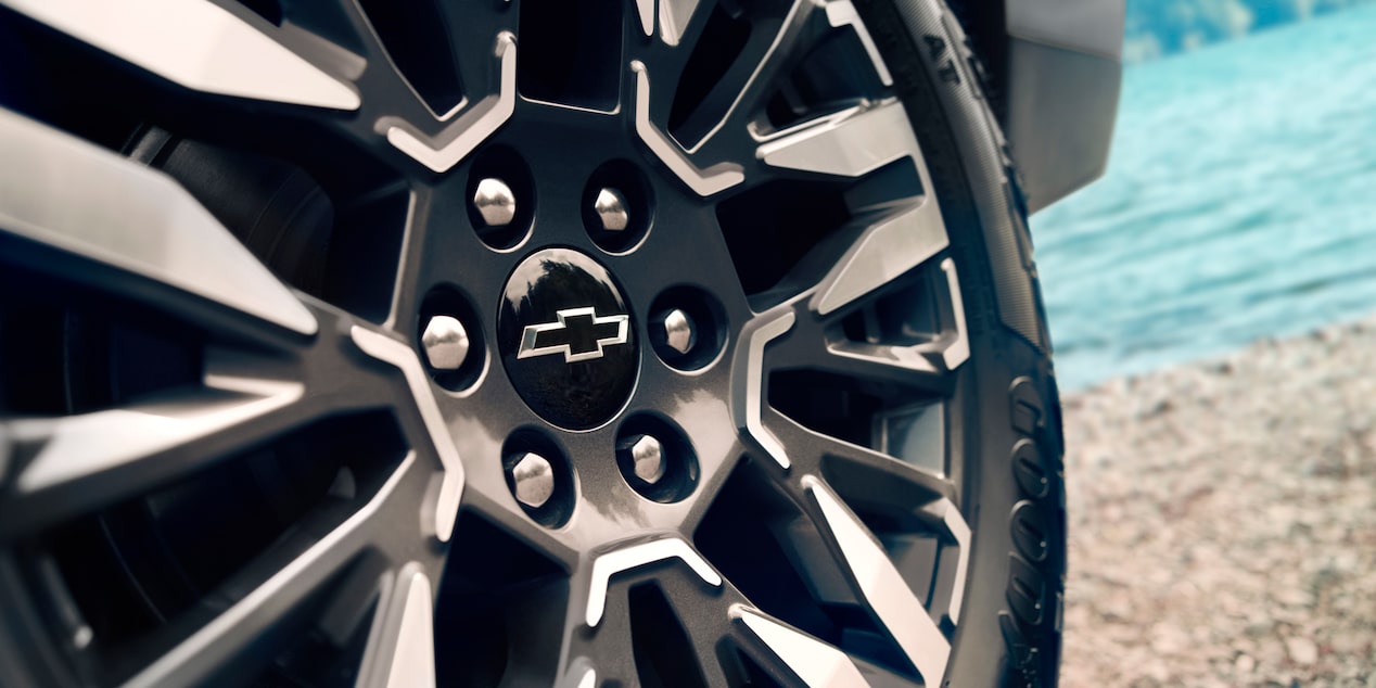 Primer plano de la llanta de aleación de la Chevrolet Suburban Z71 con el emblema de Chevrolet, junto a un paisaje de lago.