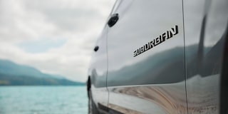Primer plano de la insignia Suburban en la Chevrolet Suburban Z71, junto a un pasiaje de lago.