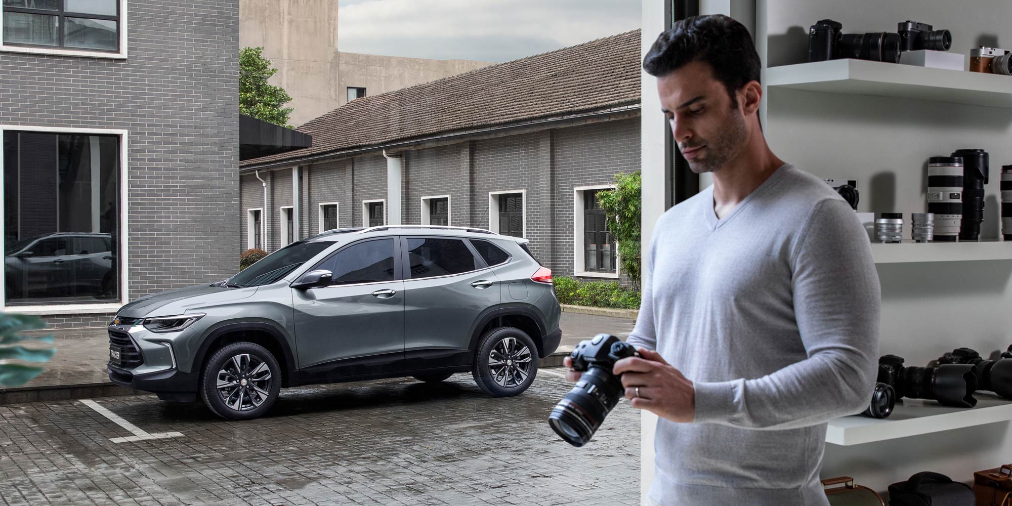 Chevrolet Tracker estacionada frente a un estudio fotográfico, mientras un hombre revisa su cámara en primer plano.