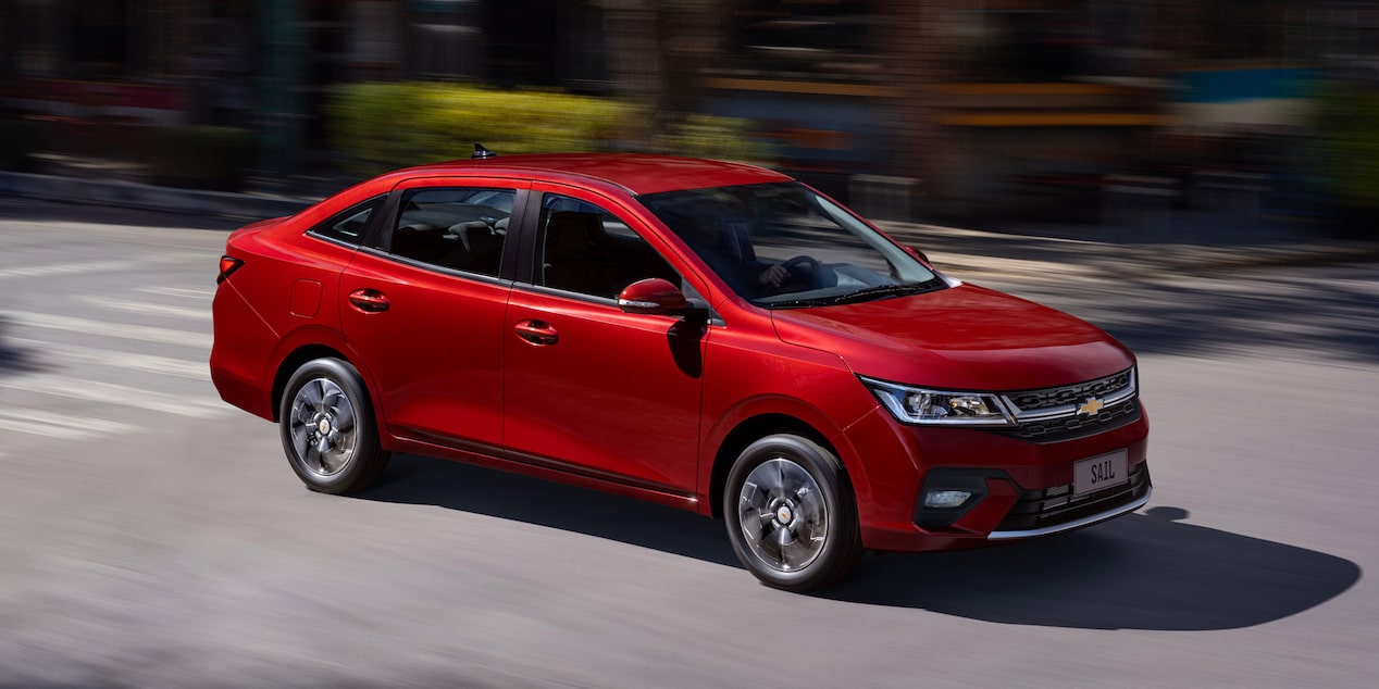 Vista lateral del Chevrolet Sail Sedán circulando por una calle en una zona urbana.