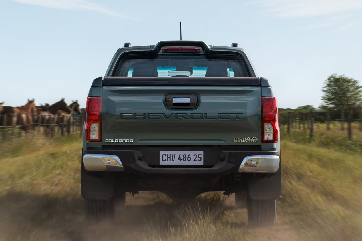 Vista trasera de una Chevrolet Colorado circulando por una calle de tierra en el campo, con caballos y árboles de fondo.
