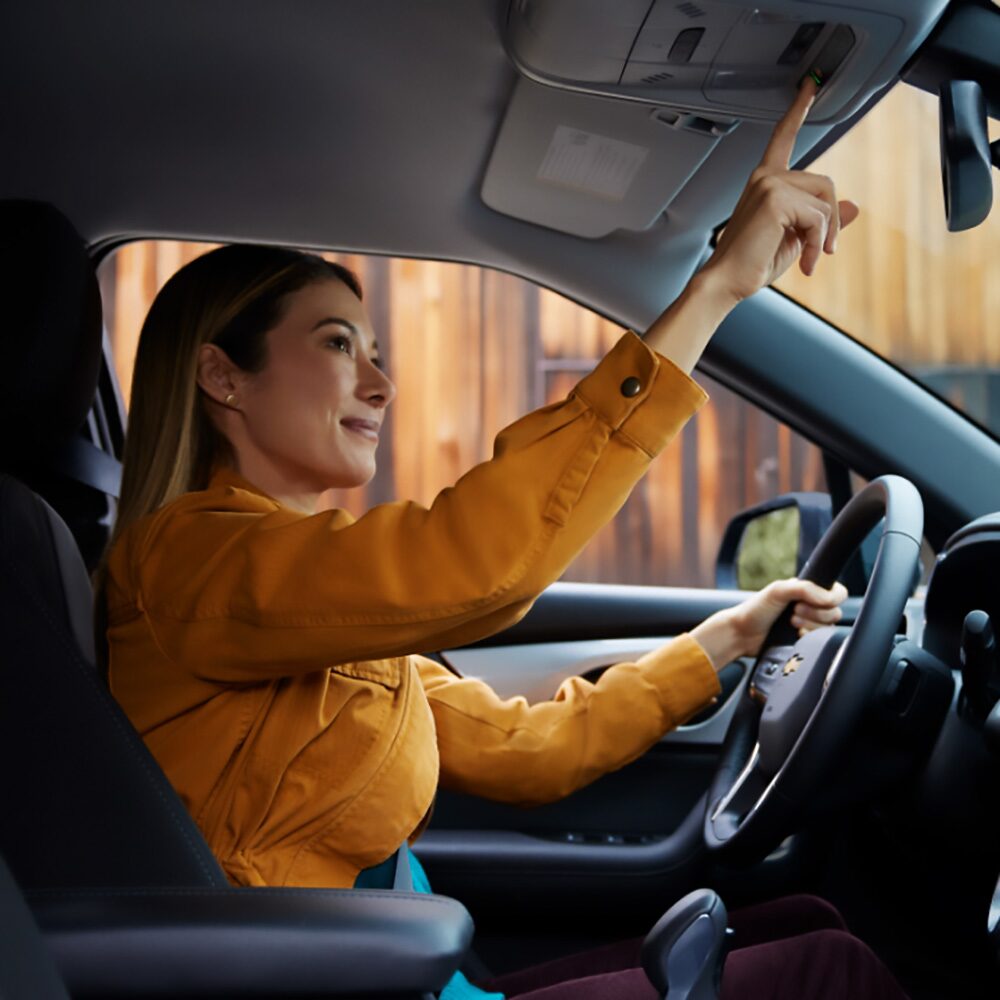 Imagen de una mujer sentada en el asiento de conductor activando el sistema OnStar desde su vehículo.